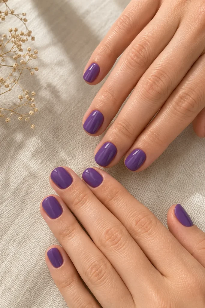 12 Ultra Violet Ideas That Look Bold and Beautiful 3 ands with a short rounded manicure in solid ultra violet polish resting on a light background