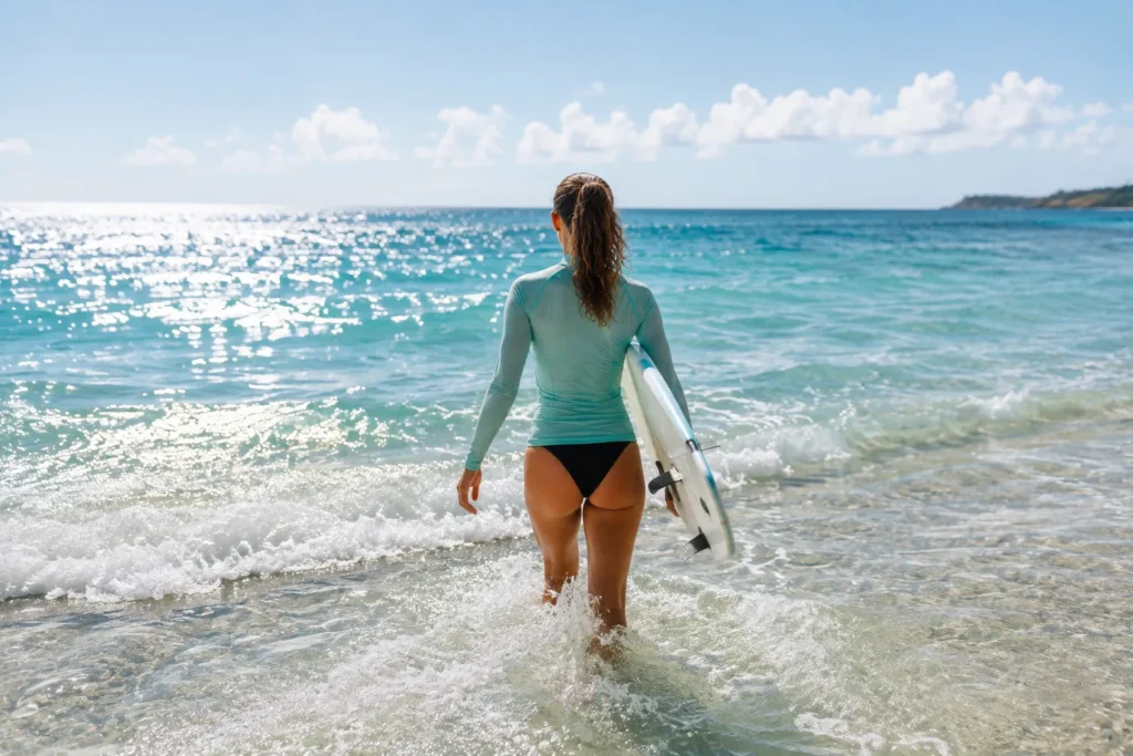 10 Beach Skincare Must-Haves for Healthy Summer Skin 11 Person in long sleeve rash guard walking into ocean waves